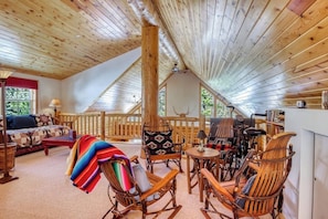 Ein gemütliches Blockhaus-Interieur mit hohen Decken, Holzwänden, einer Essecke mit Stühlen, einer Couch und einem Kamin.
