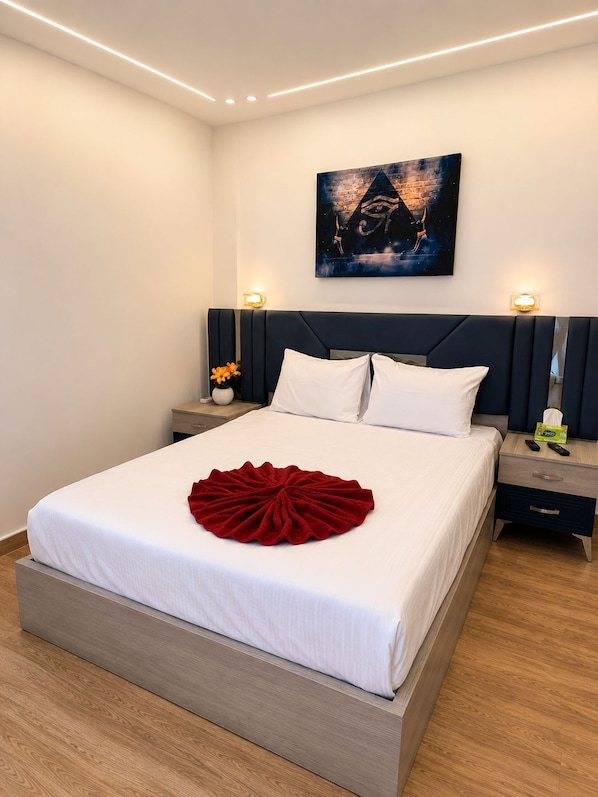 A neatly made bed with a red decorative item, a wall-mounted painting, and bedside lamps.