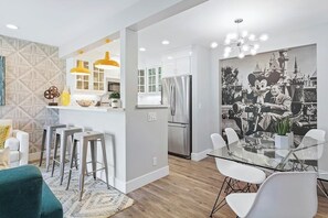 A modern kitchen with white cabinets, stainless steel appliances, and a dining area with a glass table and white chairs. - Newly renovated condo, closest walk to theme parks - pools & hot tub on-site (Anaheim)