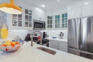 A modern kitchen with white cabinets, stainless steel appliances, and a bowl of fruit on the counter. - Newly renovated condo, closest walk to theme parks - pools & hot tub on-site (Anaheim)