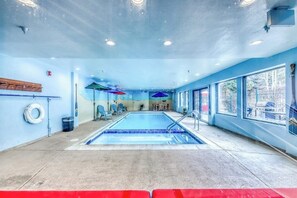 A swimming pool with a tiled floor, surrounded by windows, and a few chairs and umbrellas. - Bright and colorful studio with breathtaking mountain views (Keystone)