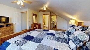 A bedroom with a large bed, a ceiling fan, a television, and a wooden dresser.