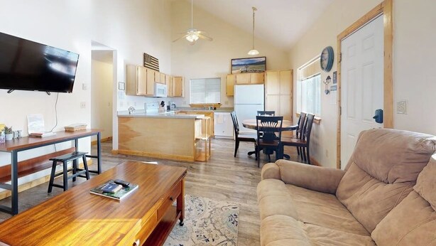 A living room with a sofa, a wooden coffee table, a TV, and a kitchen area with a dining table and chairs.