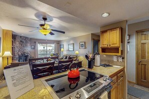A kitchen with a stove, a kettle, wooden cabinets, and a ceiling fan.