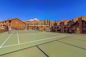 Una cancha de tenis rodeada de edificios de cabañas con una montaña al fondo.
