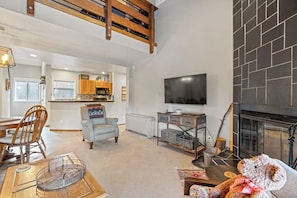 Ein Wohnzimmer mit Kamin, einem an der Wand befestigten Fernseher und einem Essbereich mit Holztisch und Stühlen.