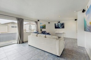A living room with a sofa, a TV, and artwork on the walls. - Spacious condo steps from the beach with full kitchen - dog-friendly (Newport Beach)
