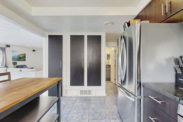 A modern kitchen with a stainless steel refrigerator, a wooden dining table, and a built-in cabinet. - Spacious condo steps from the beach with full kitchen - dog-friendly (Newport Beach)