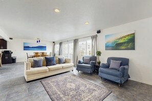 Ein Wohnzimmer mit einer Couch, zwei Sesseln, einem Teppich, einem Gemälde und Meerblick.
