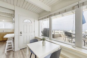 Ein Zimmer mit Esstisch, Stühlen, einer Topfpflanze, einer weißen Tür und Blick auf den Balkon mit Sitzgelegenheit.