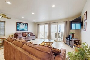 A spacious living room with a large brown sofa, a glass coffee table, and a flat-screen TV mounted on the wall. - Waterfront home with beautiful ocean views & beach access (Newport Beach)