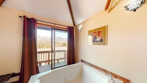 Een badkamer met een groot bad, een raam met gordijnen en een houten terras buiten.