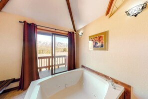 Ein Badezimmer mit einer großen Badewanne, einem Fenster mit Vorhängen und einem Holzdeck davor.