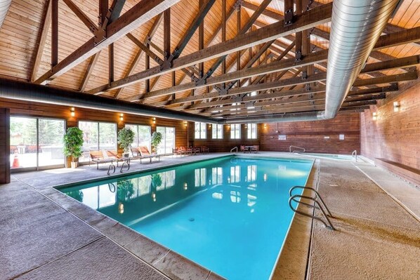 Ein Innenpool mit Holzbalken, klarem Wasser und sonnendurchfluteten Fenstern.