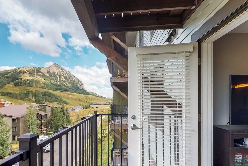 Uma varanda com vista para as montanhas, uma porta com persianas brancas e um móvel para televisão.