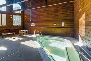Ein Holzblockhaus-Interieur mit Whirlpool, Sitzgruppe und großen Fenstern.