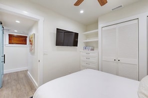 Ein Schlafzimmer mit Bett, einem an der Wand befestigten Fernseher, einem Kleiderschrank und einem Deckenventilator.
