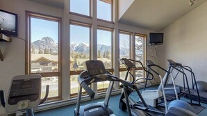 Une salle de sport équipée de tapis de course, d’un vélo d’appartement et d’un rameur, de grandes fenêtres offrant une vue sur les montagnes et d’un téléviseur fixé au mur.