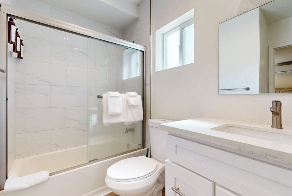 Een badkamer met een douche in een glazen cabine, een wit toilet, een wastafel met spiegel en een handdoekhouder.