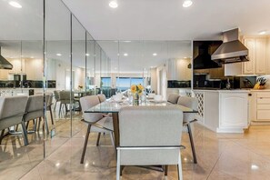 A modern kitchen with glass walls, a dining area with a table set for four, and a view of the sea. - Ocean-view condo, balcony, clubhouse, gym, pool, hot tub, snowbird haven (Newport Beach)