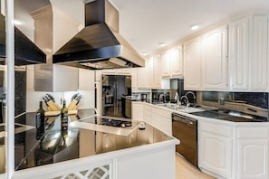 A modern kitchen with white cabinetry, a black countertop, stainless steel appliances, and a central island. - Ocean-view condo, balcony, clubhouse, gym, pool, hot tub, snowbird haven (Newport Beach)