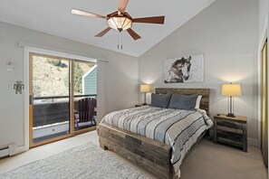 Ein Schlafzimmer mit einem Bett, zwei Nachttischen, einem Deckenventilator, einem großen Fenster und einer Glasschiebetür, die zu einem Außenbereich führt.
