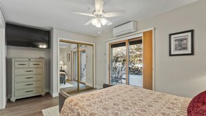 Ein Schlafzimmer mit Bett, Deckenventilator, Kommode und einer Schiebetür zu einem Außenbereich.
