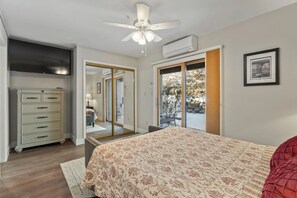 Ein Schlafzimmer mit Bett, Deckenventilator, Kommode und einer Schiebetür zu einem Außenbereich.