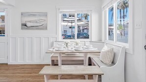 A dining area with a white table set for four, a bench, and a window with a view of the street.