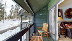 Eine Holzterrasse mit Stuhl, Tisch, einer Glastür und einer Couch mit gemustertem Kissen.