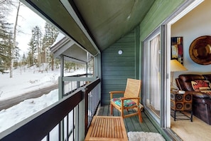 Eine Holzterrasse mit Stuhl, Tisch, einer Glastür und einer Couch mit gemustertem Kissen.