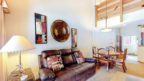 Ein Wohnzimmer mit einer Ledersofa, einem Esstisch mit Stühlen, einer Lampe und Wandbildern.