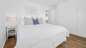 Une chambre à coucher blanche, avec un lit, une table de chevet, une lampe, un ventilateur de plafond et une armoire.