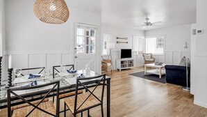 Un salon moderne comprenant un coin repas, des murs blancs, un plancher en bois et un ventilateur de plafond.