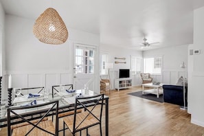 Un salon moderne comprenant un coin repas, des murs blancs, un plancher en bois et un ventilateur de plafond.