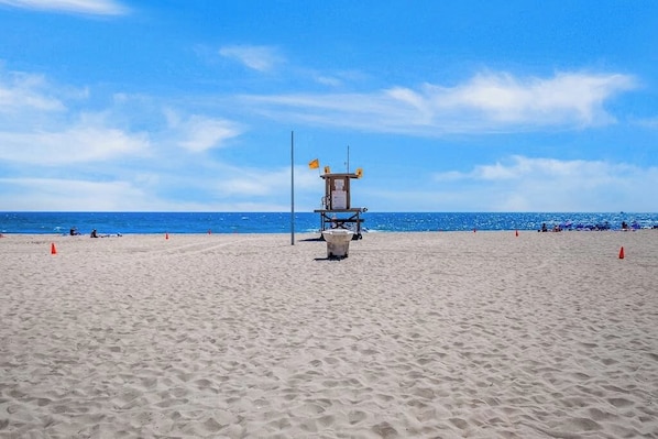 Une tour de surveillance des sauveteurs sur une plage de sable, avec l’océan en arrière-plan.