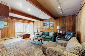 Un salón espacioso con paredes de madera, un sofá de cuero verde, un sillón de cuero negro y cojines estampados.