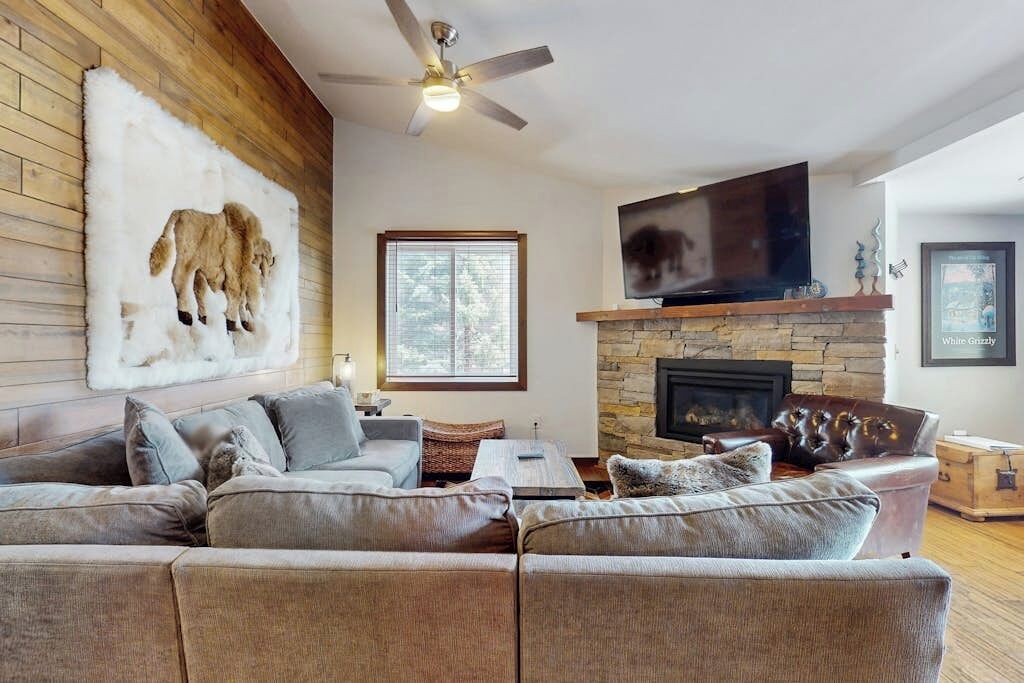 A living room with a sectional sofa, a fireplace, a mounted TV, and a ceiling fan.