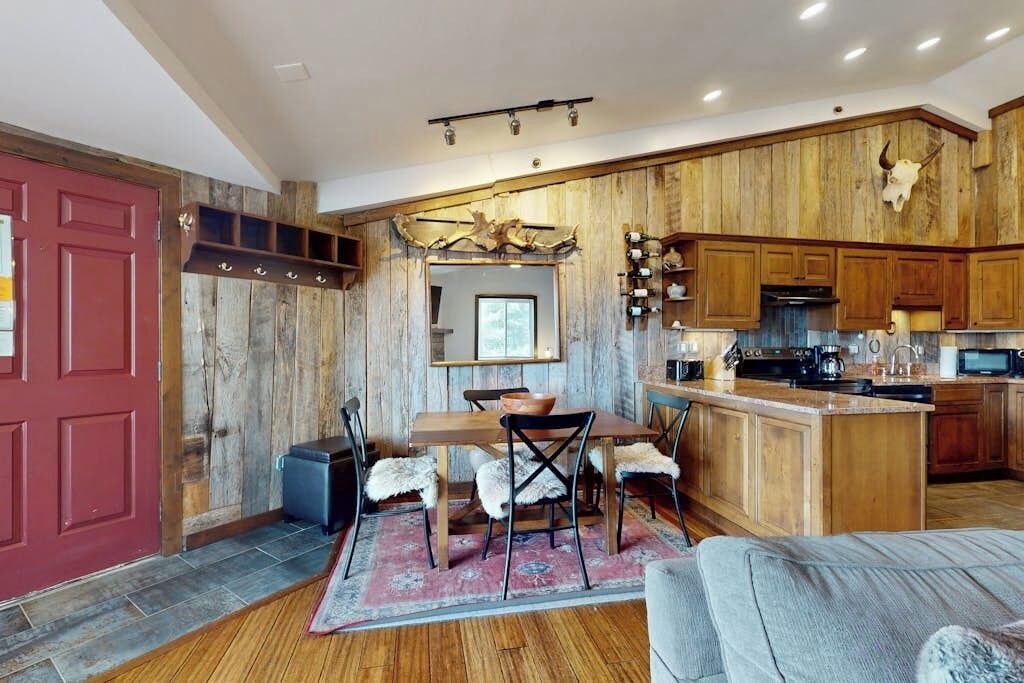 A rustic kitchen with wooden cabinets, a red door, and a dining area with a table and chairs.