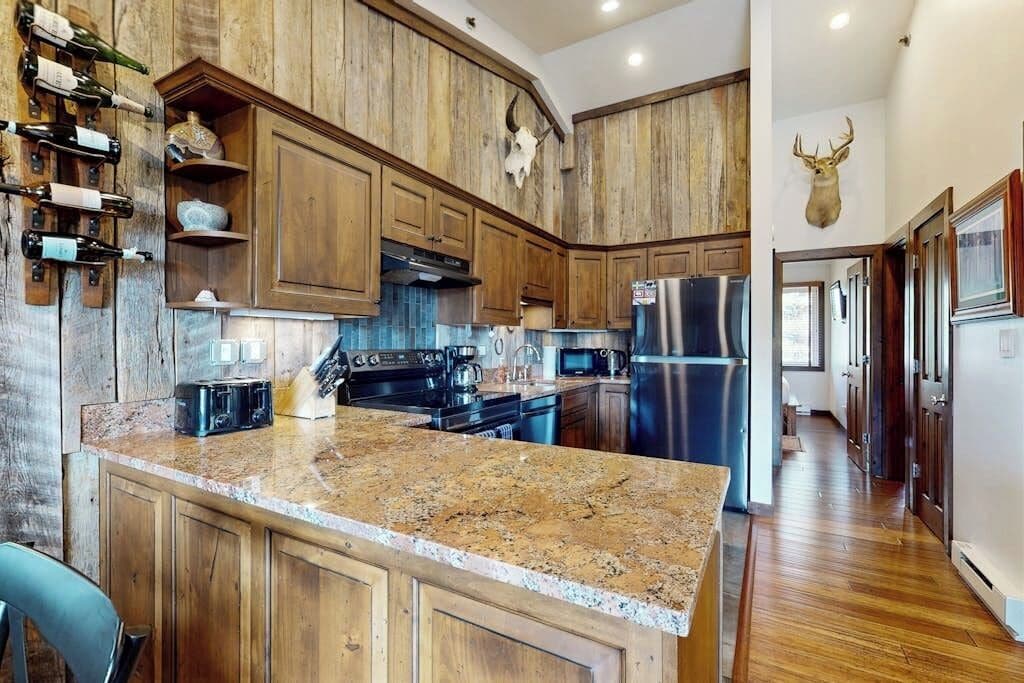 A kitchen with wooden cabinets, a granite countertop, stainless steel appliances, and a mounted deer head.