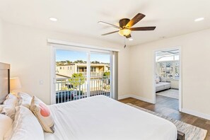 Ein Schlafzimmer mit Bett, Deckenventilator und Blick auf einen Balkon mit Geländer.