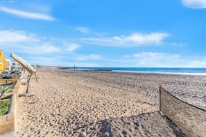 Ein Strand mit Holzlattenzaun, einem Rettungsturm und einem klaren, blauen Himmel.