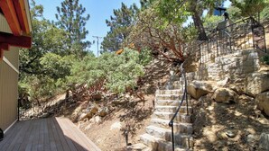 A wooden deck leading to a stone staircase with a metal railing, surrounded by trees and a building. - Upscale home with lake views, gas grill, washer/dryer, fireplace, patio, deck (Lake Arrowhead)