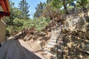 A wooden deck leading to a stone staircase with a metal railing, surrounded by trees and a building. - Upscale home with lake views, gas grill, washer/dryer, fireplace, patio, deck (Lake Arrowhead)