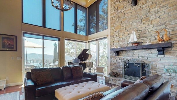 A spacious living room with a stone fireplace, large windows, and a piano. - Upscale home with lake views, gas grill, washer/dryer, fireplace, patio, deck (Lake Arrowhead)