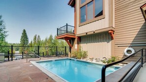 Una piscina con cubierta de madera, área cercada y un edificio con balcón.