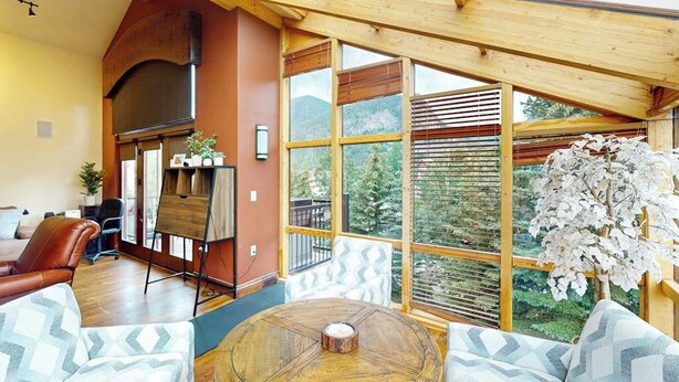 Una habitación amplia con un gran techo de madera, una mesa redonda de madera y vistas a la vegetación a través de amplios ventanales.