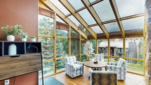 Una habitación con ventanas amplias, techo de madera y un rincón de descanso con sillas estampadas.