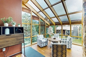 Ein Zimmer mit großen Fenstern, einer Holzbalkendecke und einer Sitzecke mit gemusterten Stühlen.