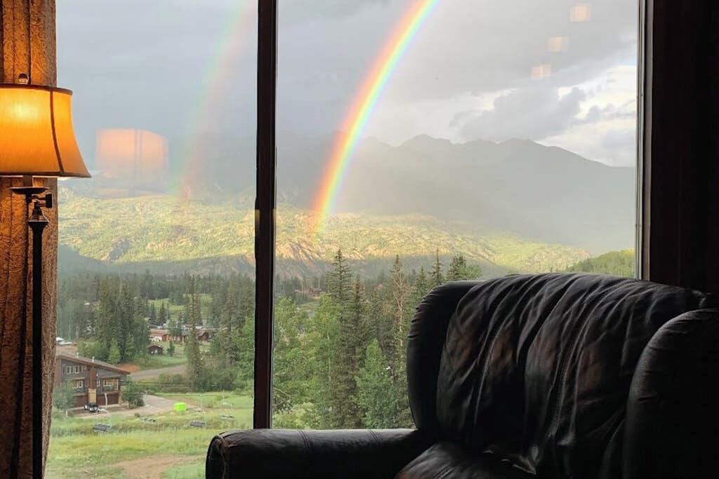 Une chambre avec vue sur un paysage montagneux et un arc-en-ciel.
